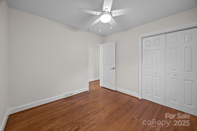 unfurnished bedroom featuring wood finished floors, a closet, ceiling fan, baseboards, and visible vents
