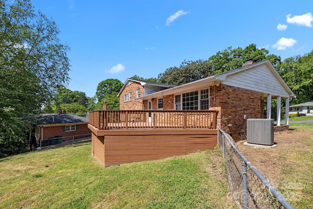 rear view of house featuring cooling unit, fence, brick siding, a wooden deck, and a lawn
