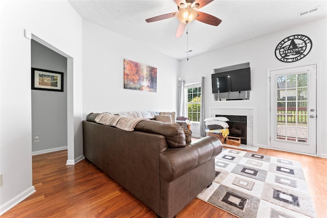 living room with wood finished floors, a fireplace with flush hearth, ceiling fan, baseboards, and visible vents
