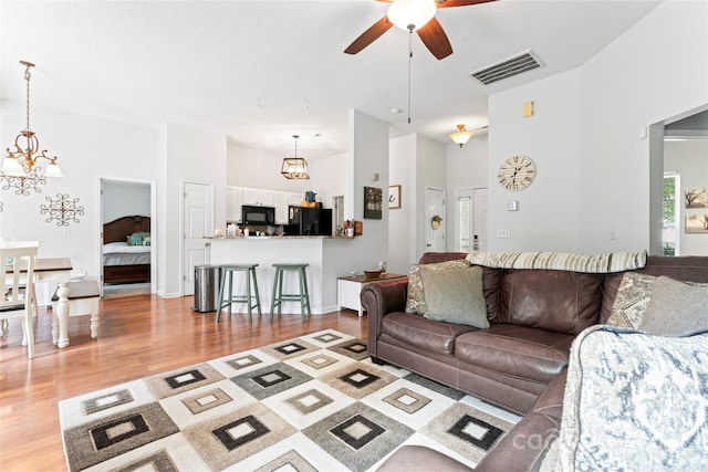 living area with a towering ceiling, wood finished floors, visible vents, and ceiling fan with notable chandelier