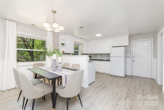 dining room featuring light wood finished floors, visible vents, and an inviting chandelier