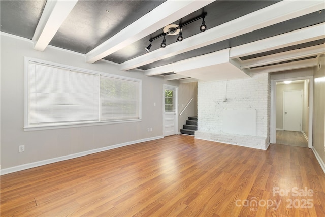 unfurnished living room featuring light wood-style floors, baseboards, beam ceiling, and stairs