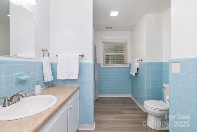full bath featuring toilet, a wainscoted wall, wood finished floors, and tile walls