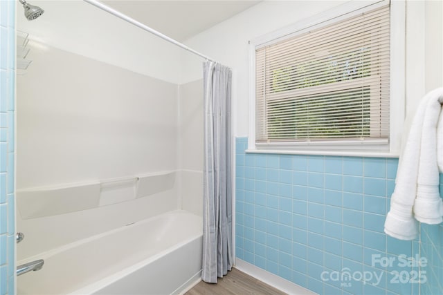 bathroom with wainscoting, wood finished floors, shower / bath combo with shower curtain, and tile walls