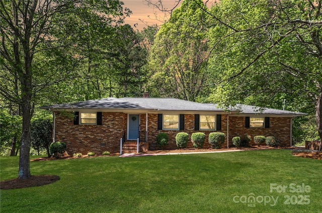 ranch-style home featuring entry steps, a chimney, brick siding, and a front yard