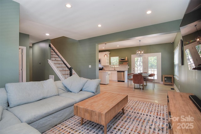 living room featuring light wood-type flooring, stairs, baseboards, a notable chandelier, and recessed lighting