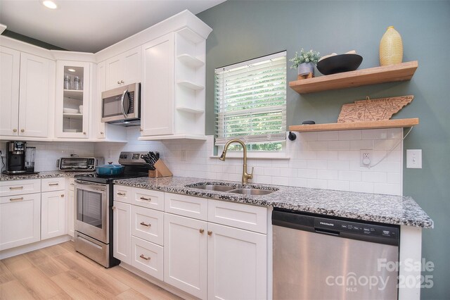 kitchen featuring appliances with stainless steel finishes, open shelves, white cabinetry, a sink, and light wood-style flooring