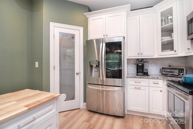kitchen featuring white cabinets, light wood finished floors, stainless steel appliances, decorative backsplash, and glass insert cabinets
