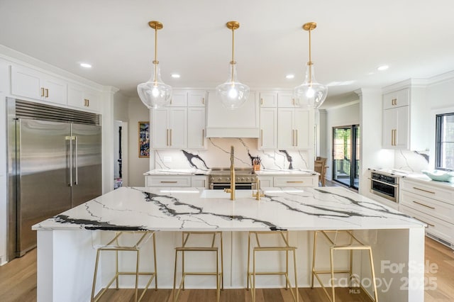 153 High Hills Dr, Mooresville, NC 28117 - kitchen featuring appliances with stainless steel finishes, a large island with sink, custom range hood, light wood finished floors, and white cabinetry