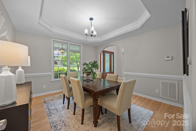 263 Fernbrook Dr, Mooresville, NC 28117 - dining space with a chandelier, arched walkways, a raised ceiling, ornamental molding, and light wood-type flooring
