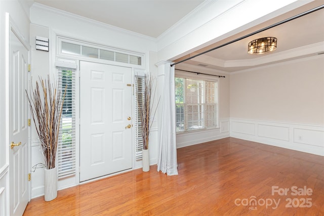 foyer featuring light wood-style flooring, ornamental molding, and a decorative wall