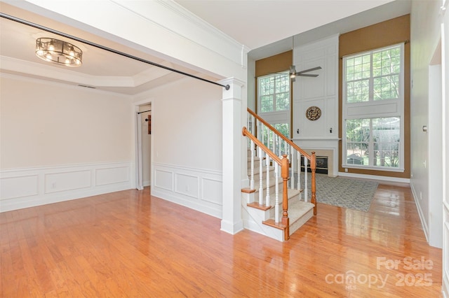 staircase with a decorative wall, wood finished floors, ornamental molding, ceiling fan, and a wainscoted wall