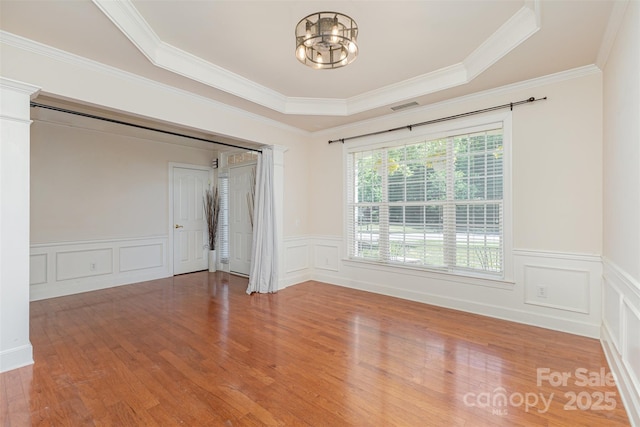 spare room featuring wood finished floors, a decorative wall, crown molding, wainscoting, and a raised ceiling