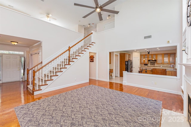 unfurnished living room featuring stairway, ceiling fan, light wood-style floors, baseboards, and a towering ceiling