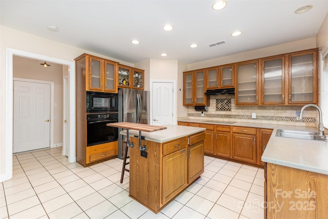 kitchen with black appliances, a sink, a center island, light countertops, and brown cabinetry