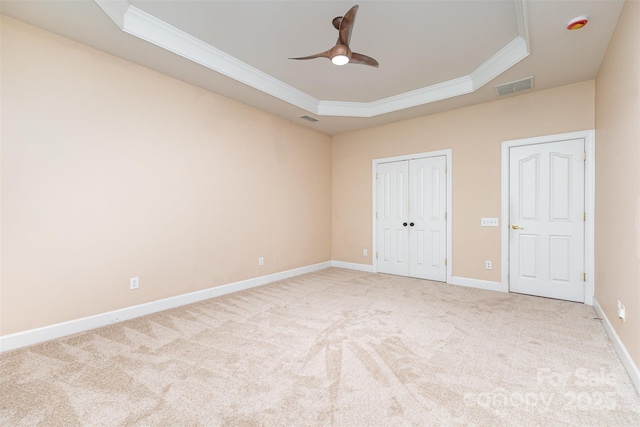 unfurnished bedroom featuring ornamental molding, a tray ceiling, carpet, baseboards, and a closet