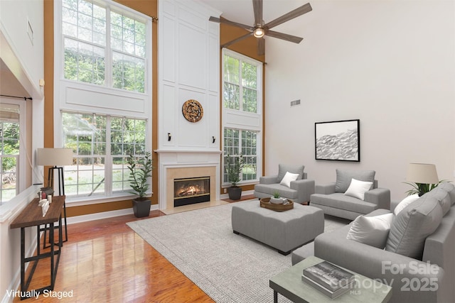 living area featuring a towering ceiling, light wood-style flooring, a ceiling fan, and healthy amount of natural light