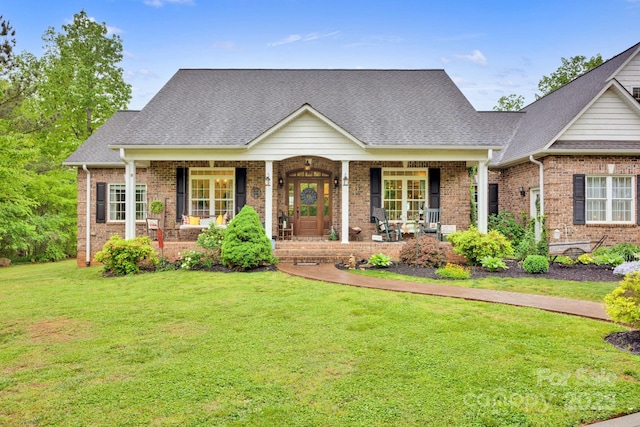 cape cod-style house with roof with shingles, covered porch, a front yard, and brick siding