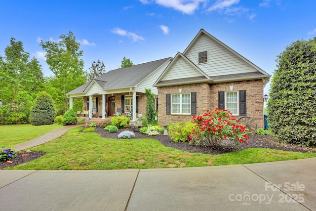 view of front of property with covered porch, brick siding, a shingled roof, and a front lawn