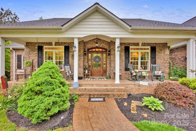 property entrance with covered porch, brick siding, and roof with shingles
