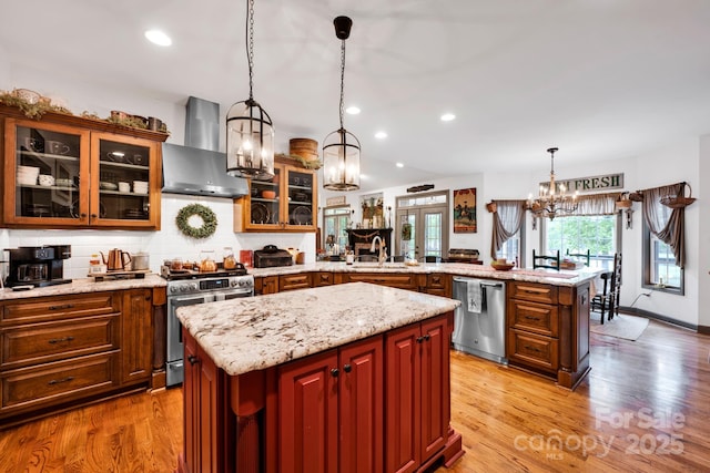 kitchen featuring stainless steel appliances, wall chimney range hood, a sink, a notable chandelier, and a peninsula