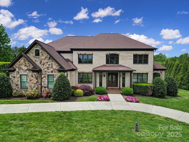 view of front of house featuring a front lawn, stone siding, and a shingled roof
