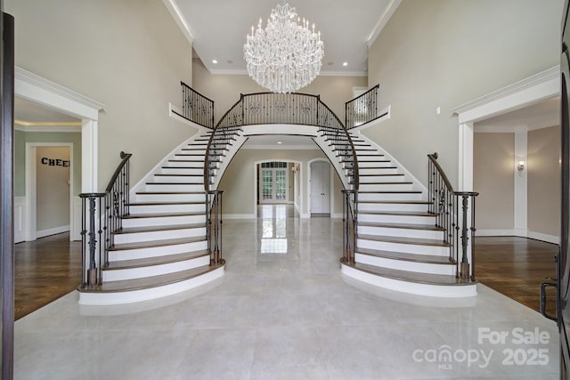 foyer entrance with stairway, a towering ceiling, ornamental molding, arched walkways, and a chandelier