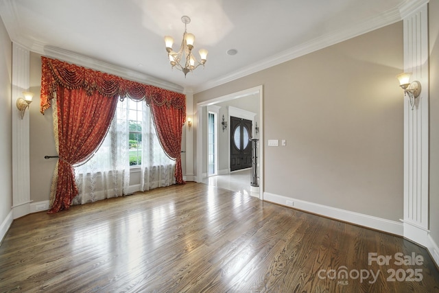 unfurnished living room with an inviting chandelier, crown molding, wood finished floors, and baseboards
