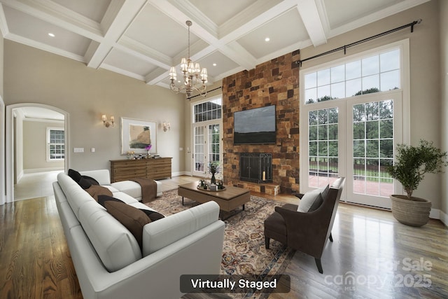 living room featuring coffered ceiling, wood finished floors, arched walkways, beam ceiling, and a chandelier