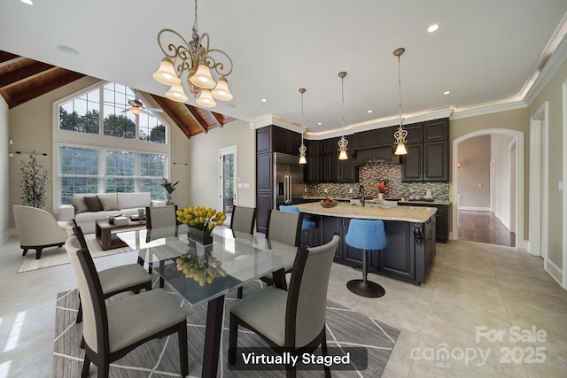 dining room with baseboards, arched walkways, vaulted ceiling, and ceiling fan with notable chandelier