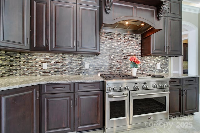 kitchen featuring premium range hood, dark brown cabinets, double oven range, and decorative backsplash