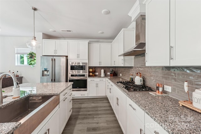 kitchen with wall chimney range hood, a sink, stainless steel appliances, white cabinetry, and visible vents