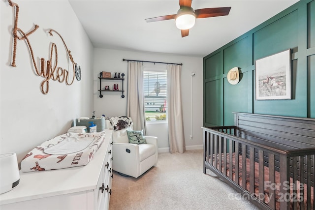 bedroom featuring light colored carpet, a nursery area, baseboards, and a ceiling fan