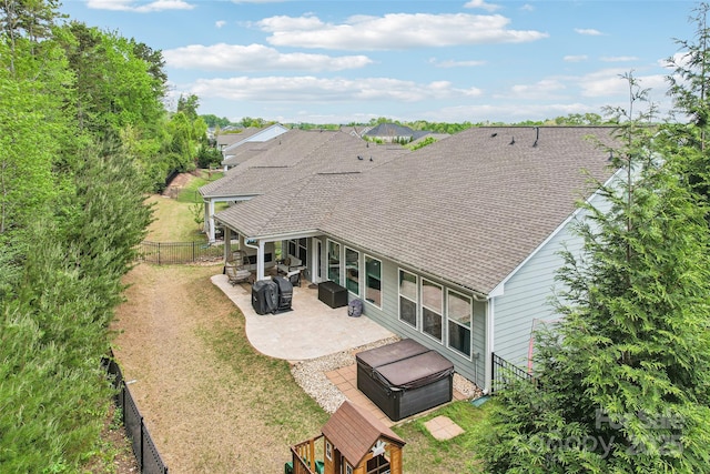 back of property featuring a hot tub, a fenced backyard, a patio, and a shingled roof