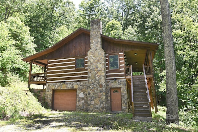 log home with an attached garage, stone siding, stairs, and a chimney