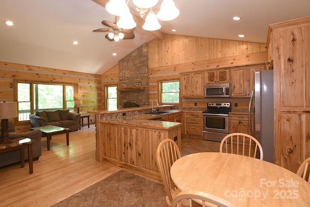 kitchen featuring a peninsula, a sink, open floor plan, wooden walls, and appliances with stainless steel finishes