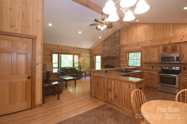 kitchen featuring open floor plan, ceiling fan with notable chandelier, wood walls, high vaulted ceiling, and appliances with stainless steel finishes