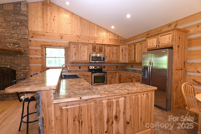 kitchen with vaulted ceiling, a sink, stainless steel appliances, a kitchen bar, and a peninsula