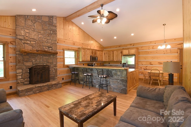 living area with a stone fireplace, beam ceiling, light wood-style flooring, high vaulted ceiling, and ceiling fan with notable chandelier