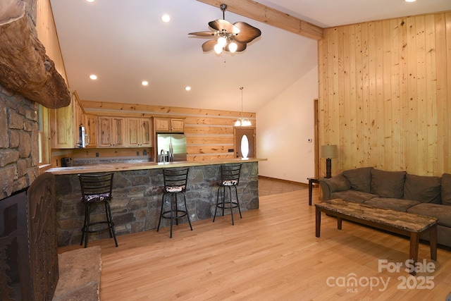 kitchen featuring a ceiling fan, a kitchen breakfast bar, vaulted ceiling with beams, stainless steel appliances, and light wood-style flooring