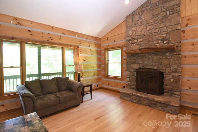 living room with vaulted ceiling, wood finished floors, wooden walls, and a stone fireplace