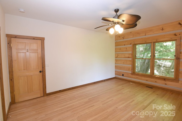 empty room featuring wood walls, a ceiling fan, light wood-style flooring, baseboards, and visible vents