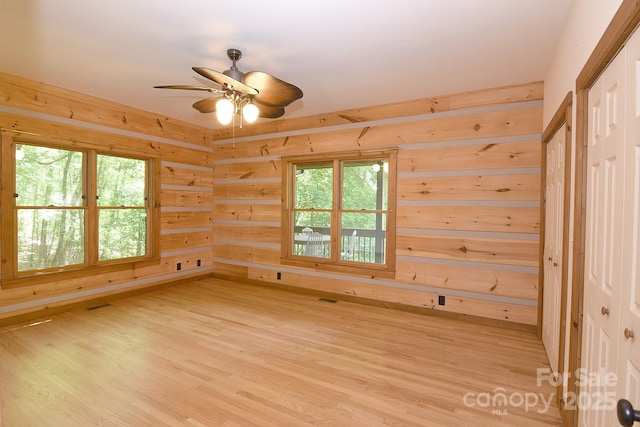 spare room with ceiling fan, a wealth of natural light, wood walls, and light wood-type flooring