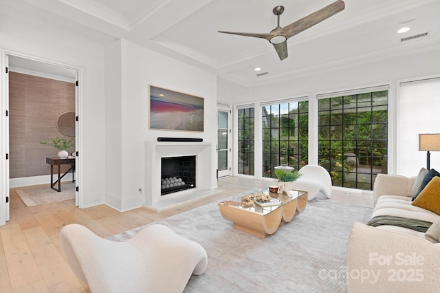 living room with a ceiling fan, visible vents, beam ceiling, a fireplace with raised hearth, and hardwood / wood-style floors