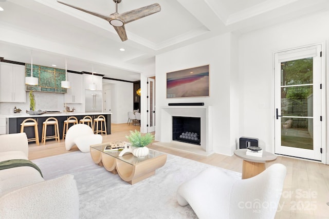 living area featuring ceiling fan, beamed ceiling, a fireplace with raised hearth, light wood-style floors, and recessed lighting