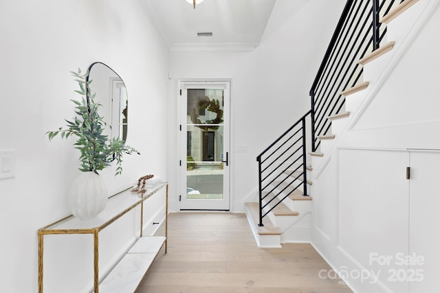 foyer featuring light wood-style floors, crown molding, stairs, and visible vents
