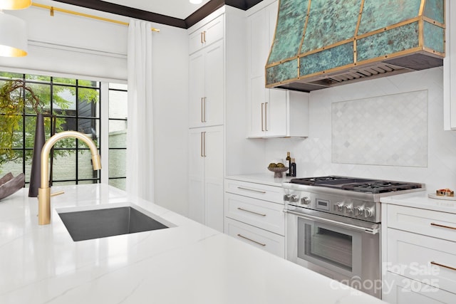 kitchen featuring custom exhaust hood, high end stainless steel range oven, white cabinets, a sink, and backsplash