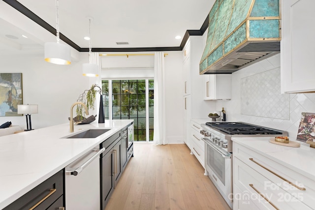 kitchen featuring decorative backsplash, ventilation hood, high end stove, a sink, and decorative light fixtures