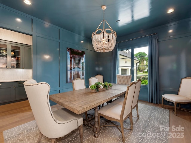 dining room featuring recessed lighting, a decorative wall, light wood-type flooring, and a chandelier