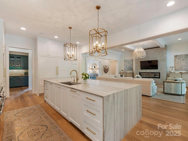 kitchen with white cabinets, a notable chandelier, light stone counters, and a sink